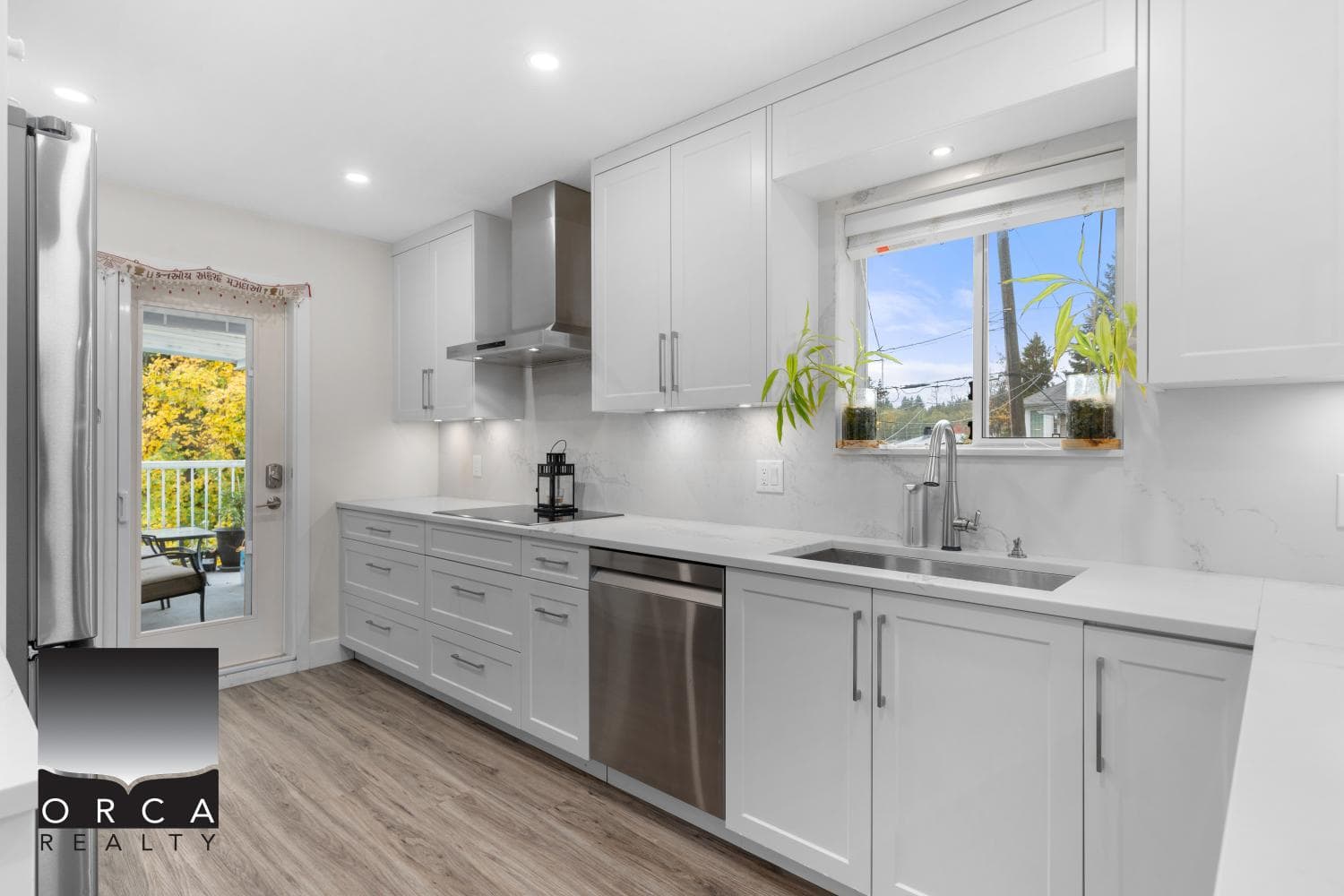 Bright modern white kitchen with stainless steel appliances, large window with greenery view, new cabinetry, and a sliding door leading to outdoor space, perfect for Vancouver Island homes.