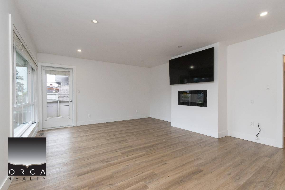 Spacious and modern living room with hardwood flooring, large windows, and a sleek fireplace with a mounted flat-screen TV, ideal for Vancouver Island homebuyers.
