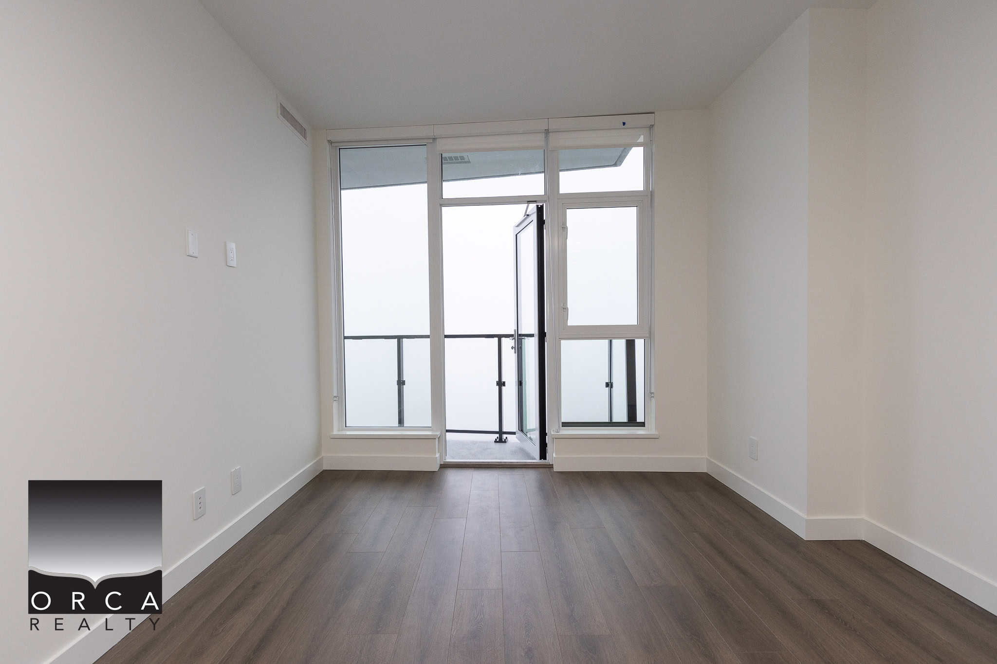 14 Bright modern apartment interior with large glass door leading to balcony, hardwood flooring, minimalist design, ideal for urban living in Vancouver, real estate listing by Orca Realty Inc.