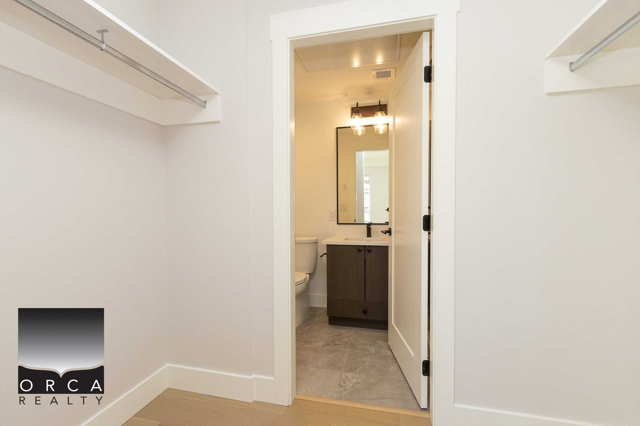 Bright empty walk-in closet with built-in shelves and hanging rods, leading to a bathroom with modern fixtures, showcasing a clean and spacious interior ideal for Vancouver real estate listings.