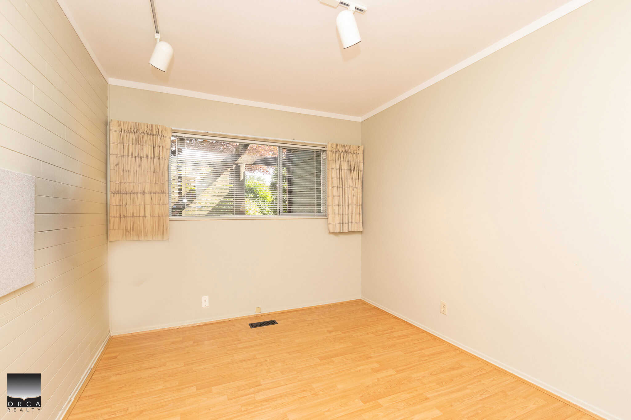 Wood flooring in a bright, vacant living room with beige walls and a large window with curtains, ideal for Vancouver real estate listings.