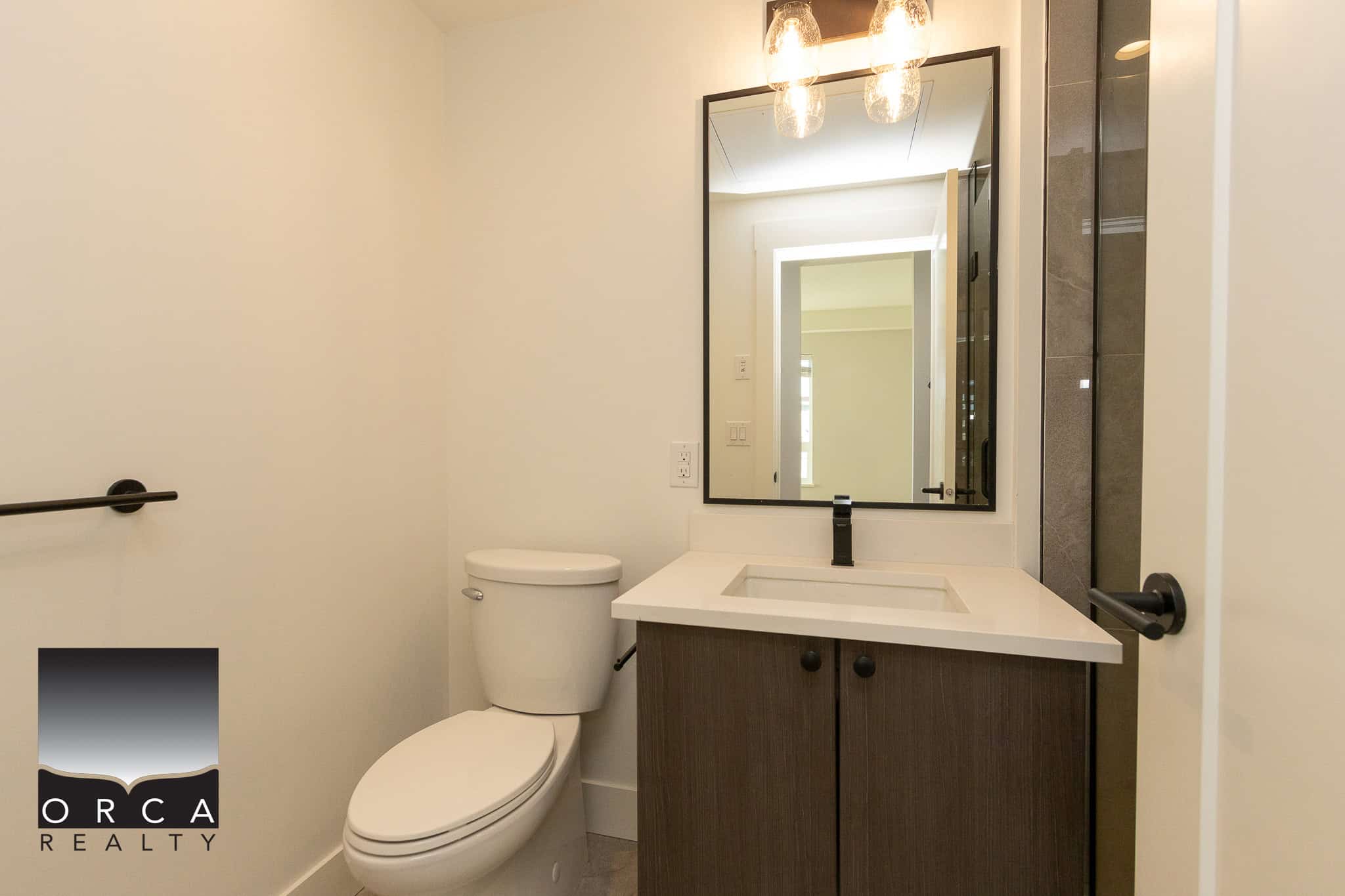 Modern bathroom with white toilet, sleek vanity with white countertop, black faucet, large mirror, minimalist design, neutral tones, ideal for rental or residential property in Vancouver.