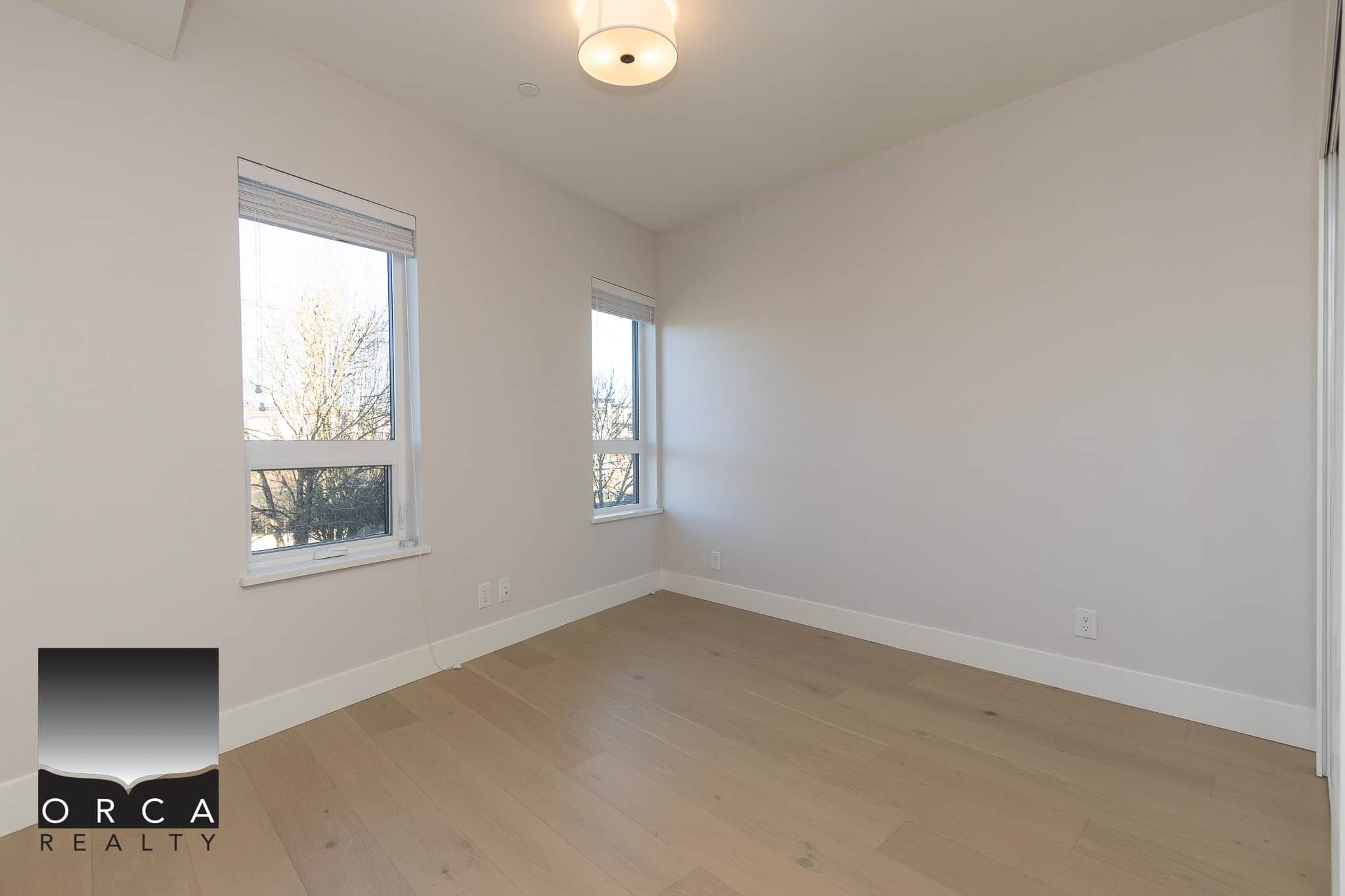 Bright empty bedroom with large windows and hardwood flooring, ideal for Vancouver homebuyers seeking modern, airy living spaces.