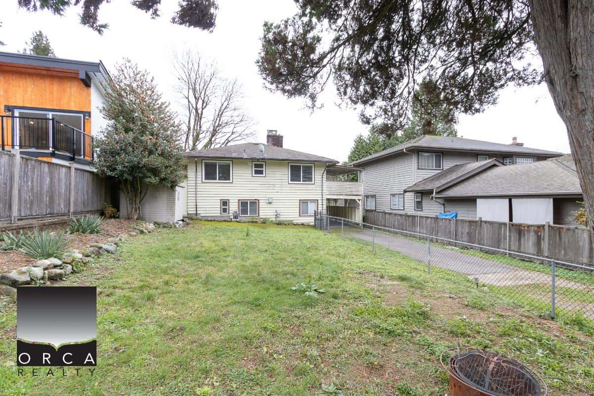 Spacious backyard with green lawn, surrounding wooden fences, mature trees and neighboring houses, ideal for outdoor activities and family gatherings in a Vancouver-area residential property.