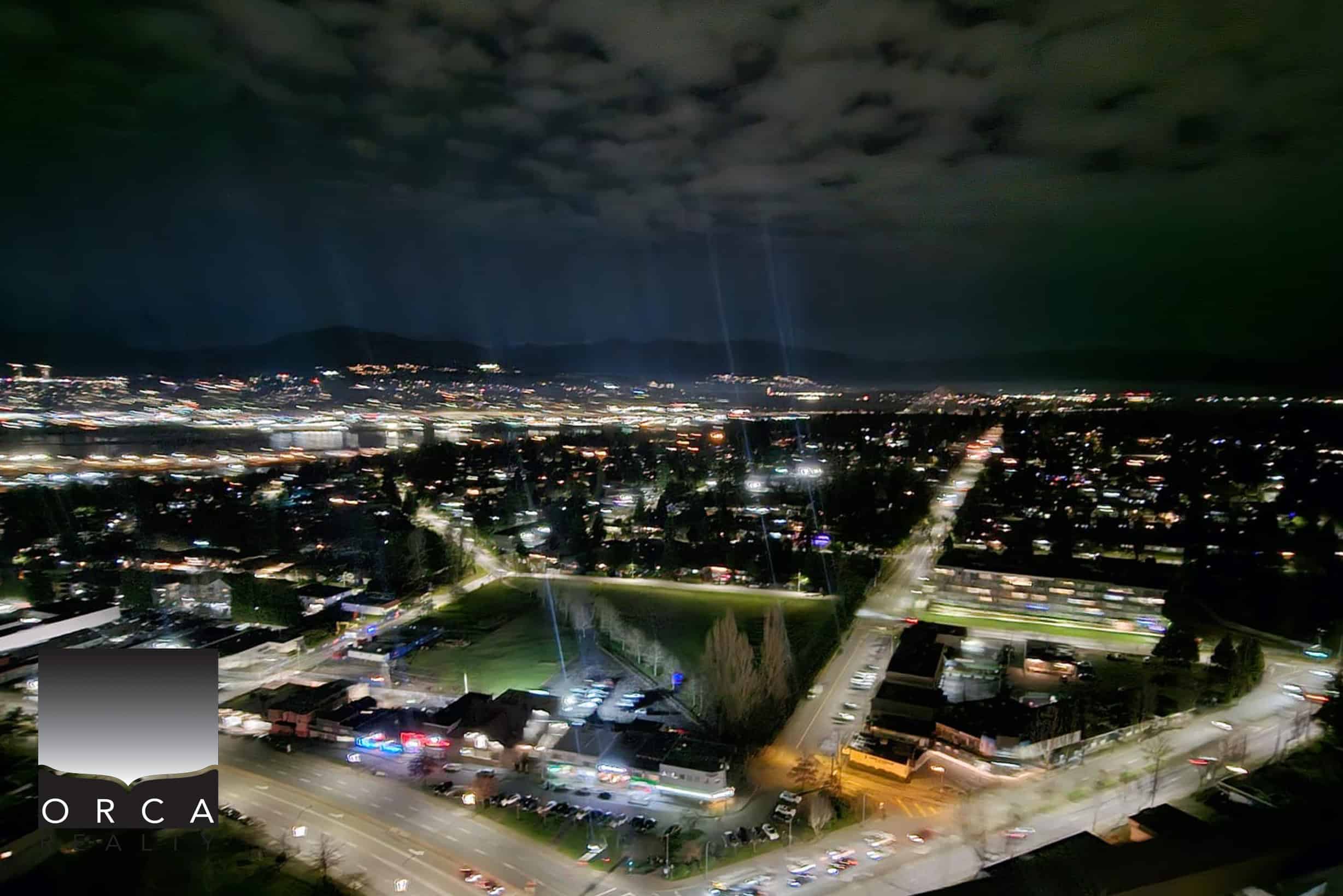 18 Night aerial view of a cityscape showcasing vibrant lights, residential neighborhoods, and a scenic mountain backdrop, representing prime real estate opportunities in the local community.