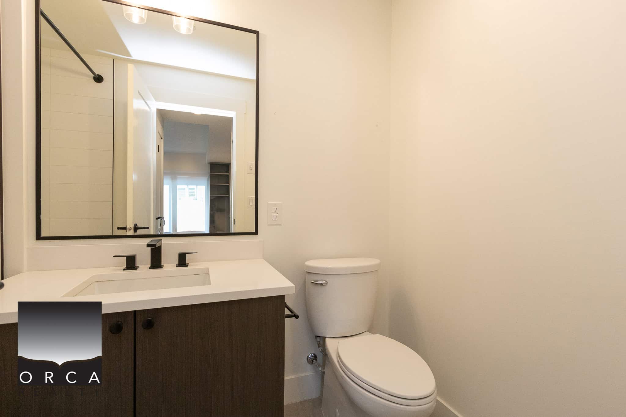 Modern bathroom with white walls, contemporary vanity, black fixtures, and a large mirror, showcasing clean and stylish design in Vancouver real estate.