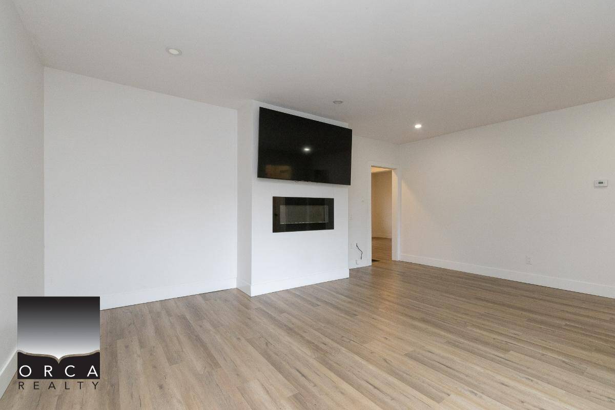 Bright empty living room with modern fireplace, wall-mounted TV, hardwood floors, and open space, ideal for Vancouver Island property buyers seeking contemporary homes.