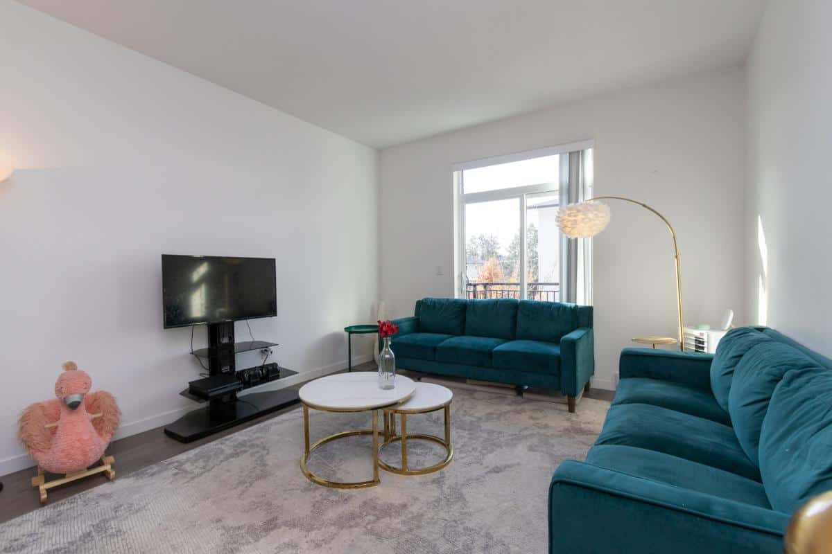 Contemporary living room with teal sofas, modern decor, and large window, showcasing upscale home interior from Orca Realty Inc. in Vancouver, BC.