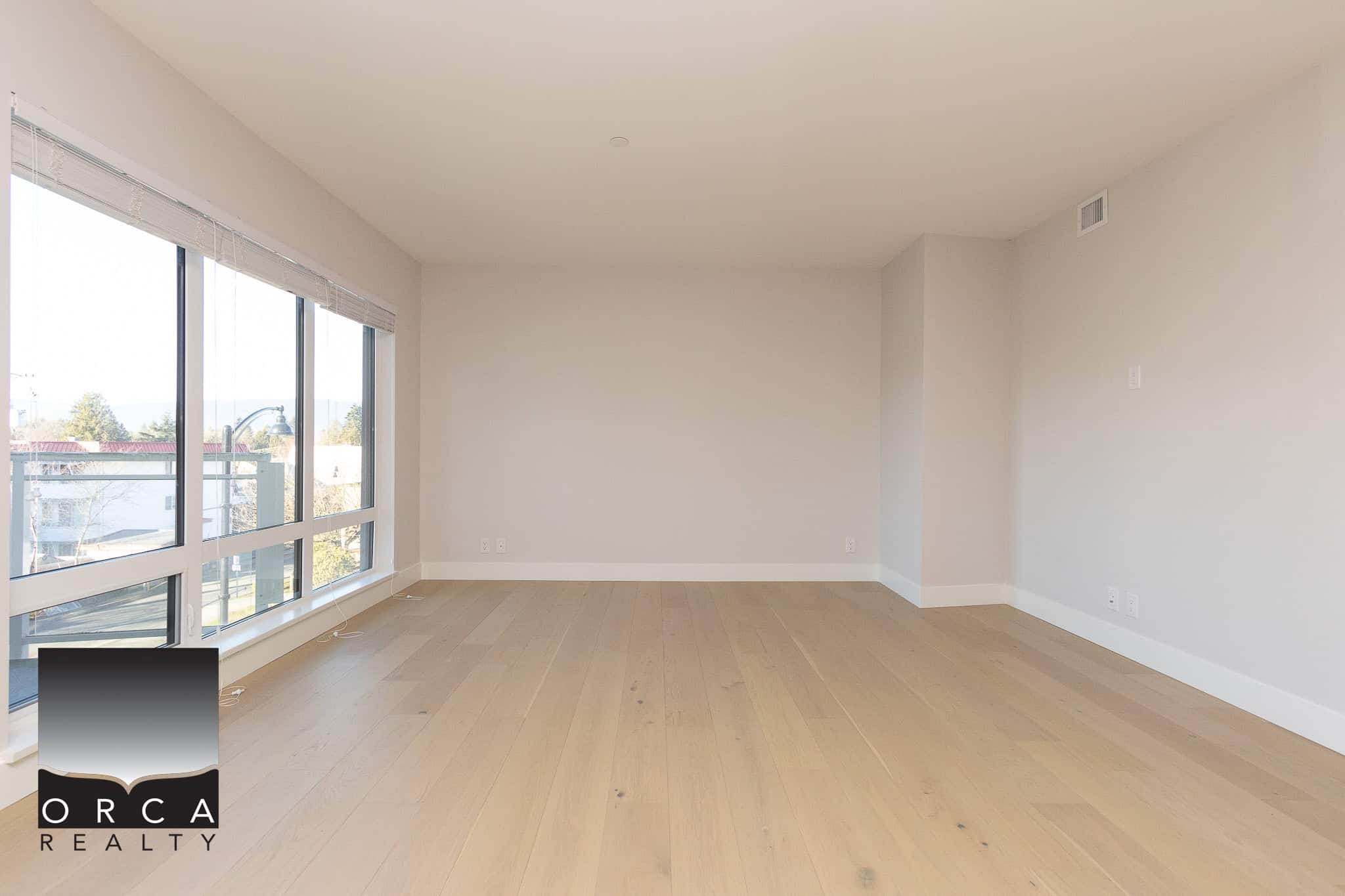 Bright, empty living room in a modern Vancouver-area condo with large windows, hardwood flooring, and neutral walls, perfect for real estate buyers seeking contemporary or luxury properties.