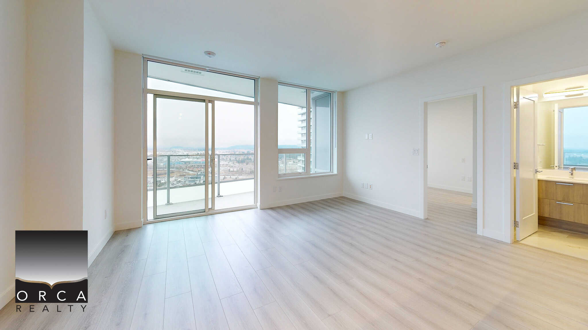 Bright modern living room with large windows and balcony access in a high-rise Vancouver condo. Features light wood flooring, white walls, and scenic city views.