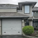 Spacious two-car garage with beige sectional door, brick accents, and a landscaped front yard featuring a neatly trimmed green bush and pink flowers, located in a modern residential property.