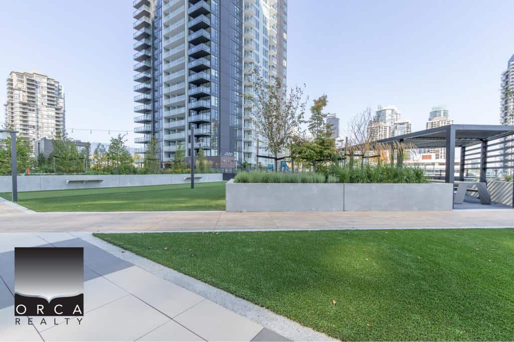 Modern urban rooftop park with lush greenery, sitting area, and scenic city views in Vancouver's high-rise residential buildings.