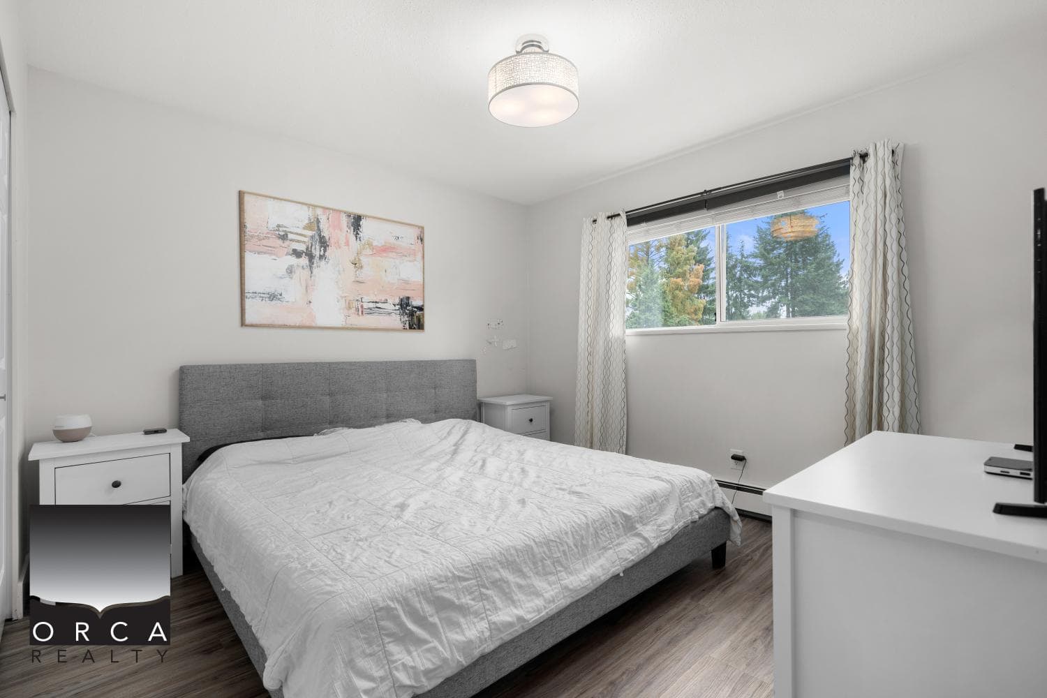 Bright modern bedroom with large window, white walls, and minimalist decor, showcasing a comfortable space perfect for real estate listings or home staging by Orca Realty.
