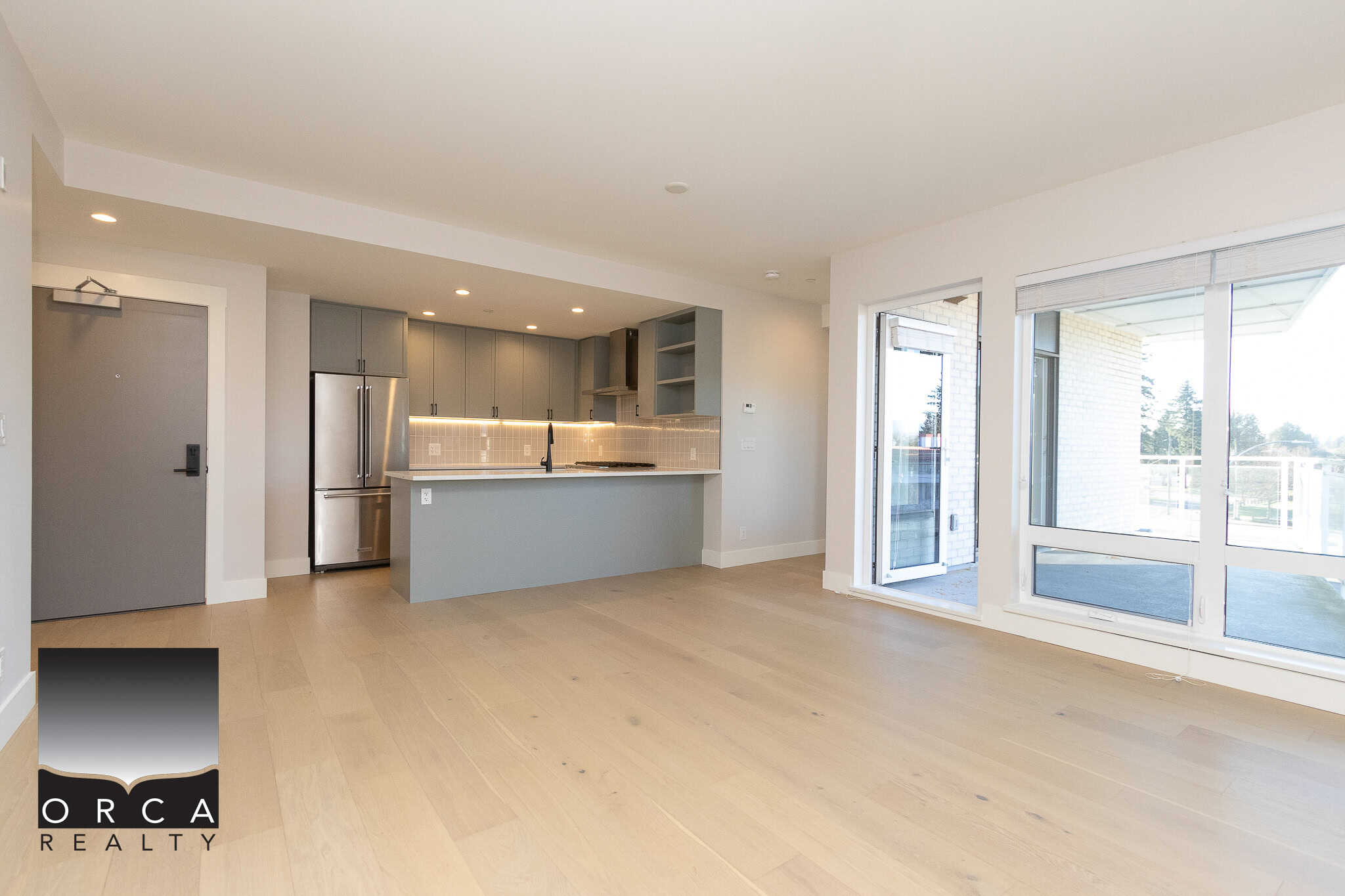 Modern open-concept kitchen and living space in a contemporary condo listing by Orca Realty Inc., featuring sleek cabinetry, stainless steel appliances, and balcony access.