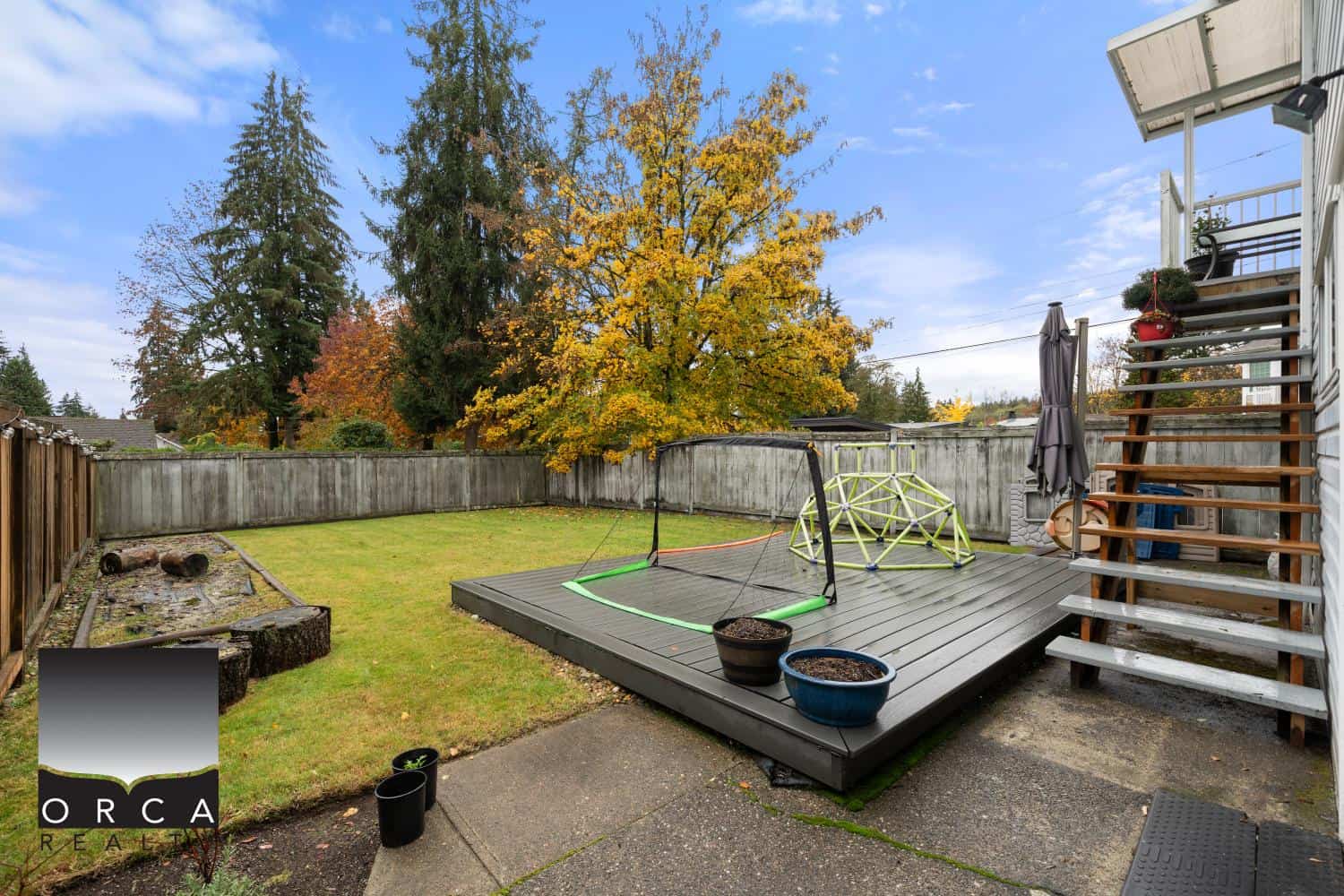 Bright backyard featuring a wooden deck, children's play area, mature trees with vibrant fall foliage, and a fenced yard, perfect for family outdoor activities and outdoor living.
