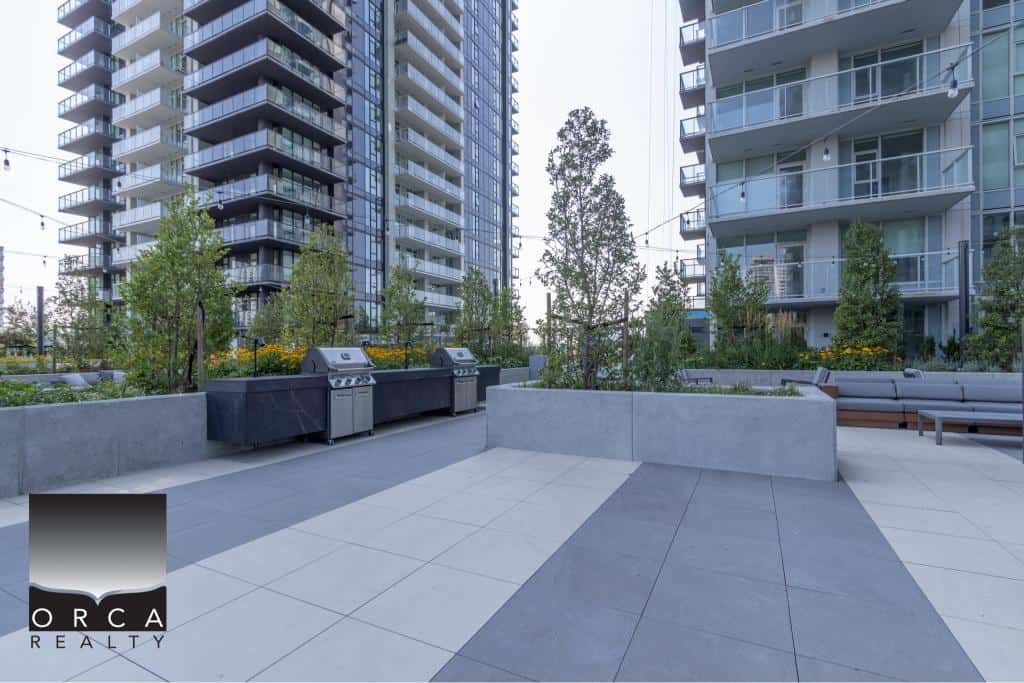 Modern outdoor rooftop patio with gas grills, contemporary seating, landscaped planters, and high-rise residential buildings in Vancouver, BC. Perfect for relaxation and social gatherings.