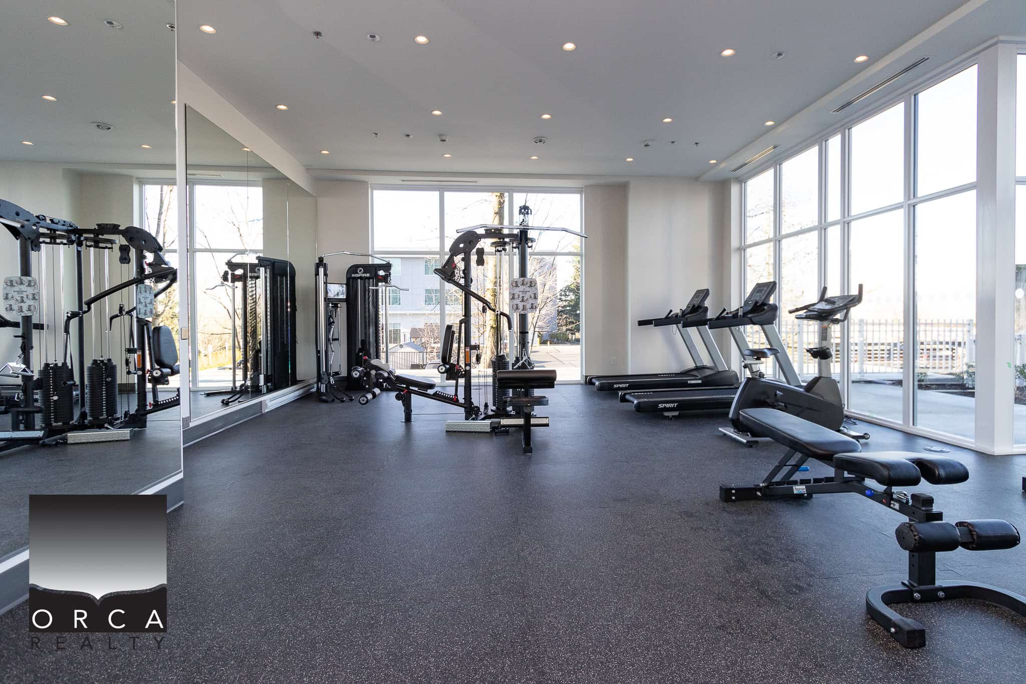 Modern indoor gym with exercise equipment, cardio machines, and free weights at Orca Realty Inc. property, perfect for health-conscious residents.