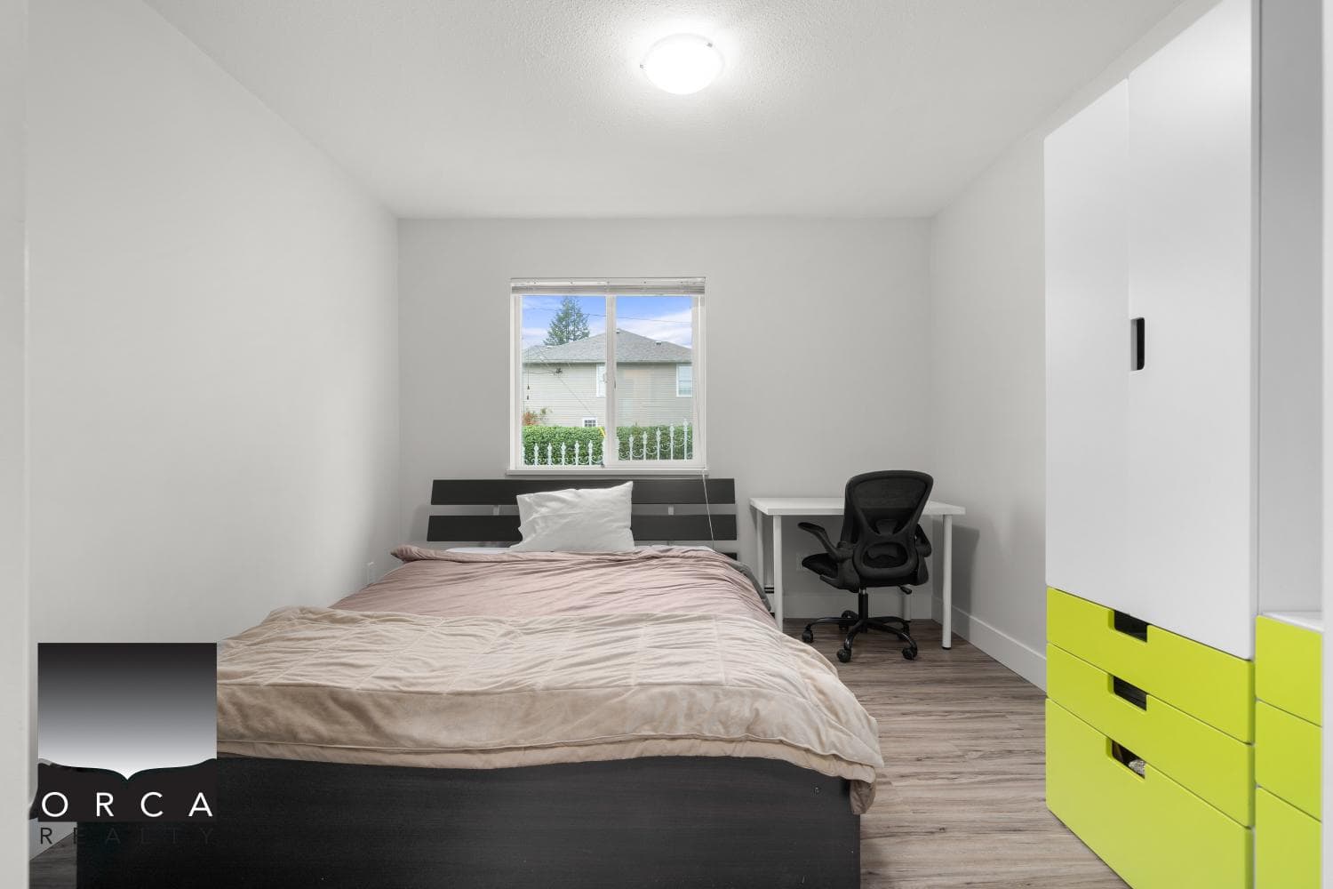Cozy bedroom with modern decor, white walls, and natural light, featuring a bed, black office chair, and contemporary yellow storage drawers, ideal for Vancouver real estate buyers.
