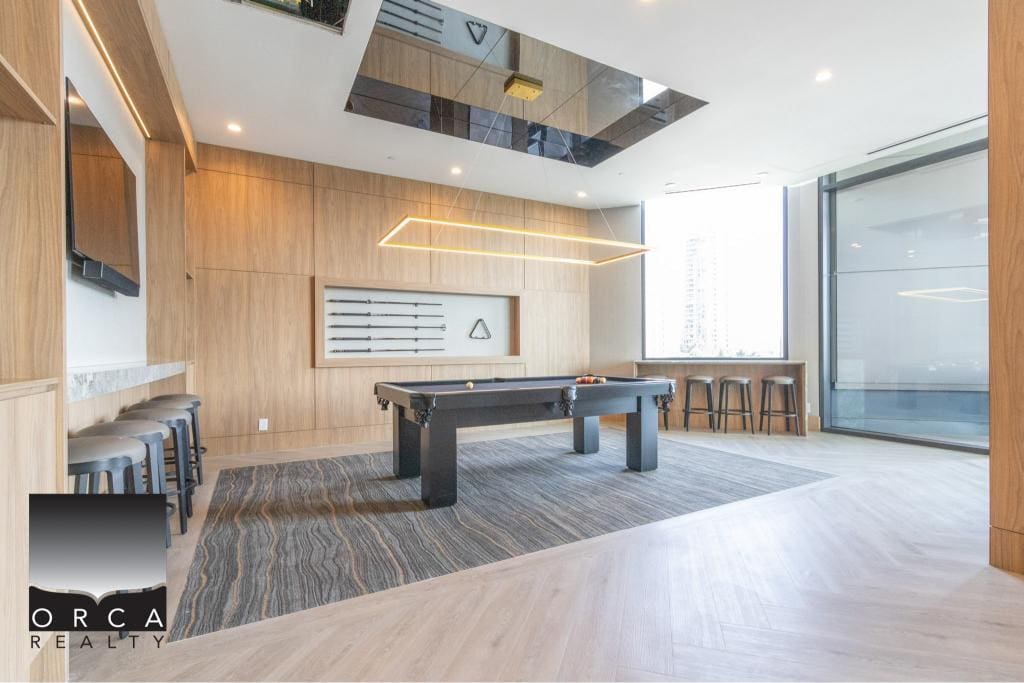 Modern indoor recreational space with billiards table, wall-mounted TV, stylish lighting, and seating area, ideal for relaxation and socializing at Orca Realty Inc.