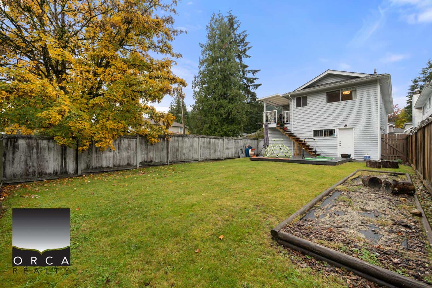 Spacious backyard of a family home with lush green lawn, mature trees with fall foliage, wooden fence, and outdoor play area, ideal for outdoor living and family activities in Vancouver BC.