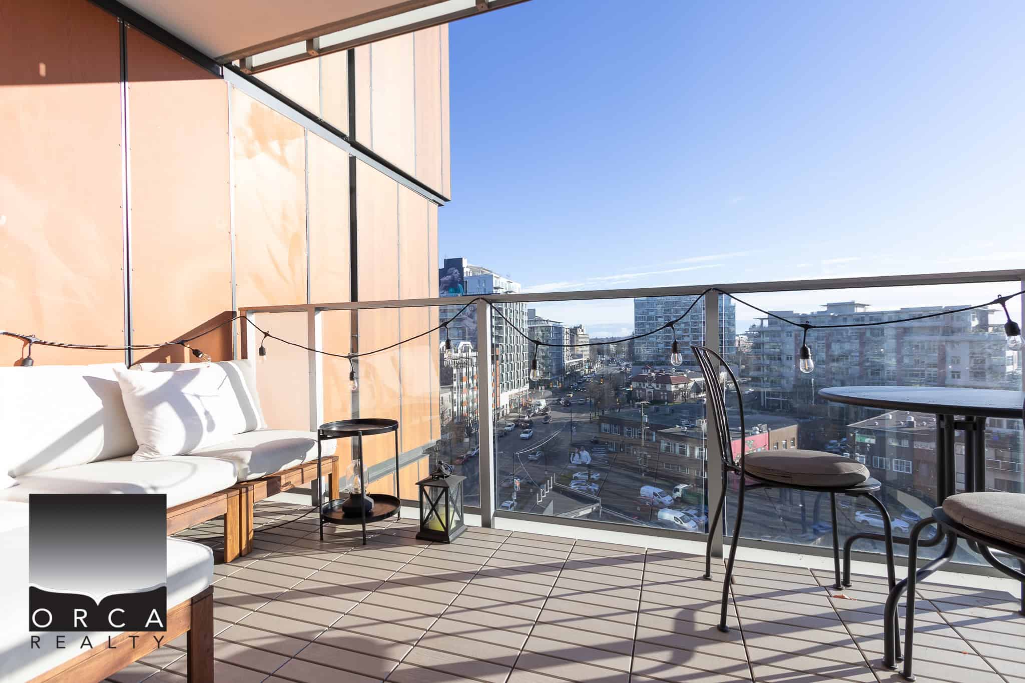 Bright urban balcony with seating and string lights, showcasing city views in Vancouver, BC; ideal for relaxed outdoor living and entertaining in a modern condo.