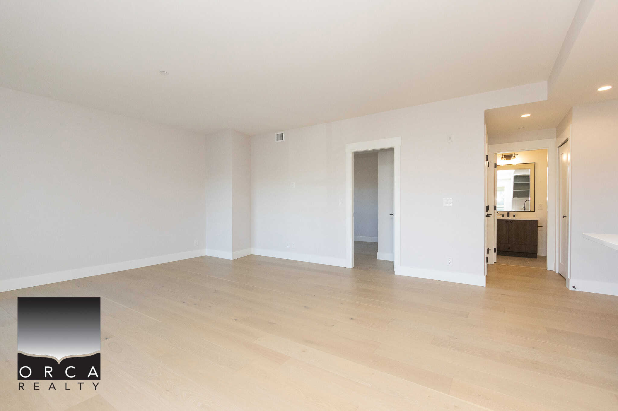 Spacious modern living room with light hardwood floors, bright white walls, and an open floor plan, ideal for showcasing luxurious properties offered by Orca Realty Inc.