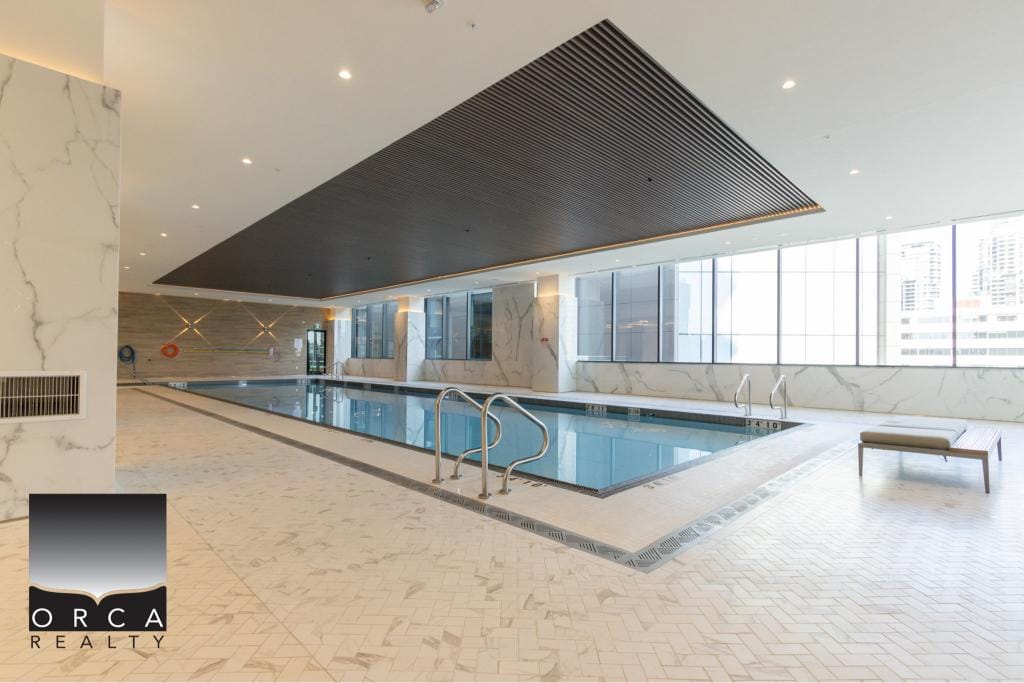 Luxurious indoor swimming pool at Orca Realty Inc. office building, featuring modern design, large windows with city views, and high-end amenities for relaxation and fitness.