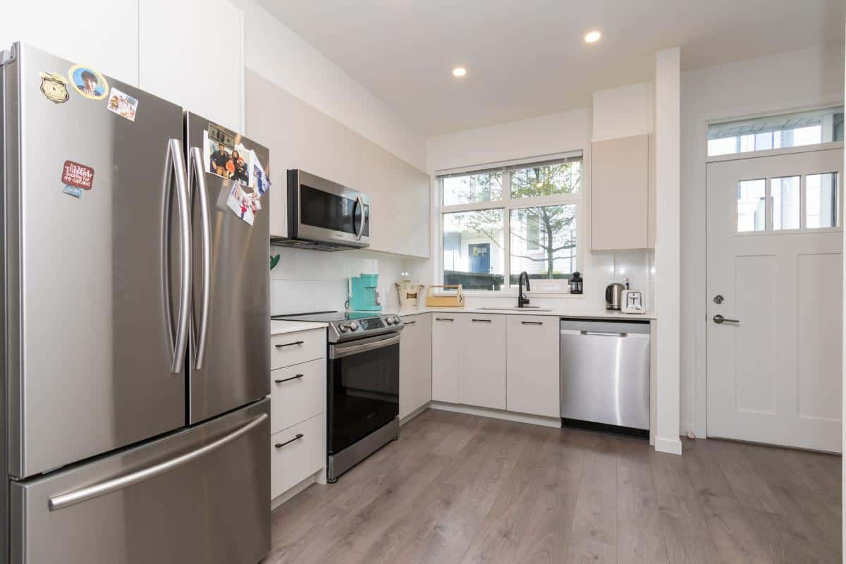Stainless steel refrigerator, oven, microwave, and dishwasher in modern white kitchen with natural light, ideal for BC real estate and Vancouver homebuyers.