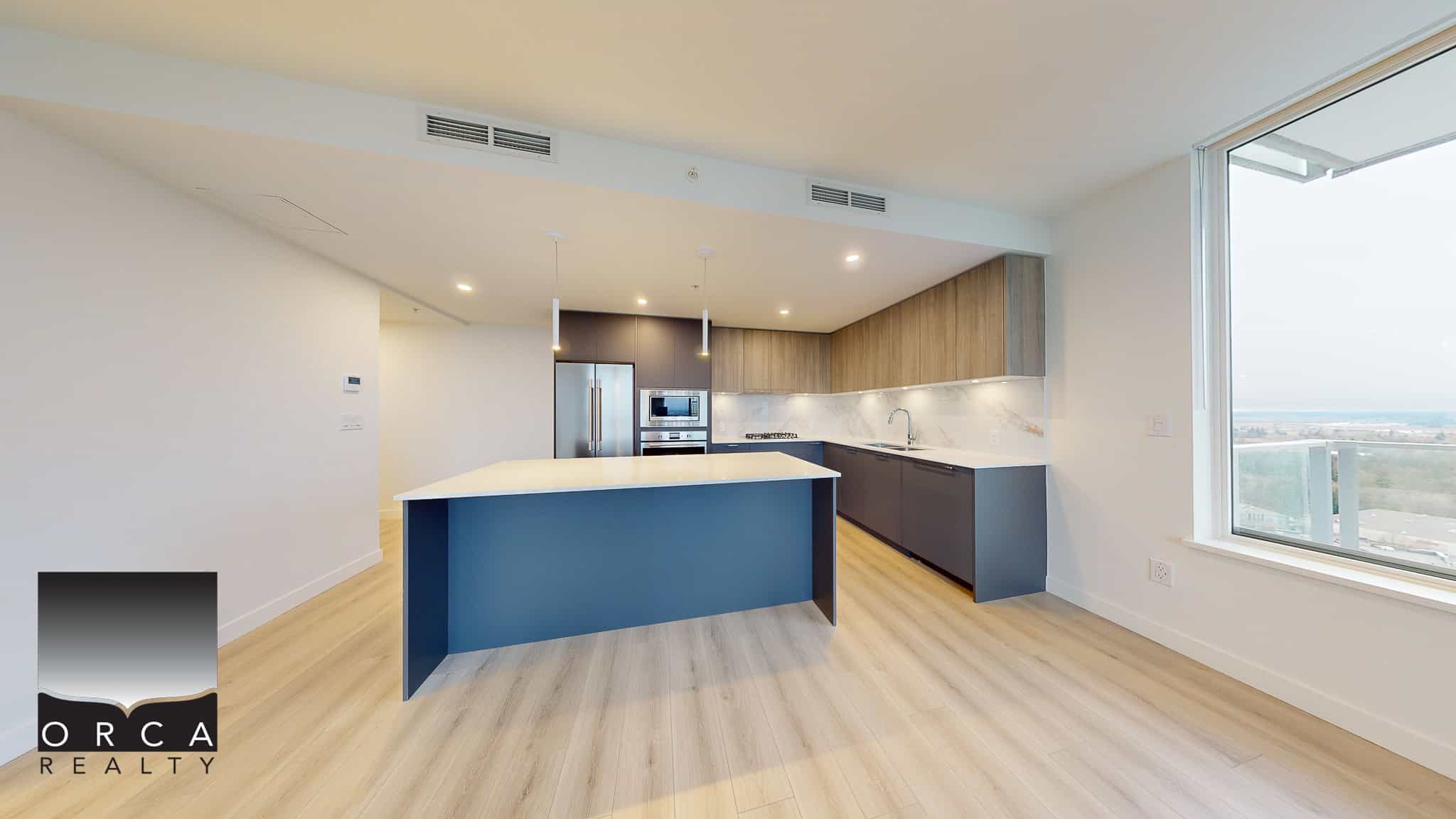 Contemporary modern kitchen in a high-rise condo with an island, stainless steel appliances, wooden cabinetry, and large windows with city and ocean views.