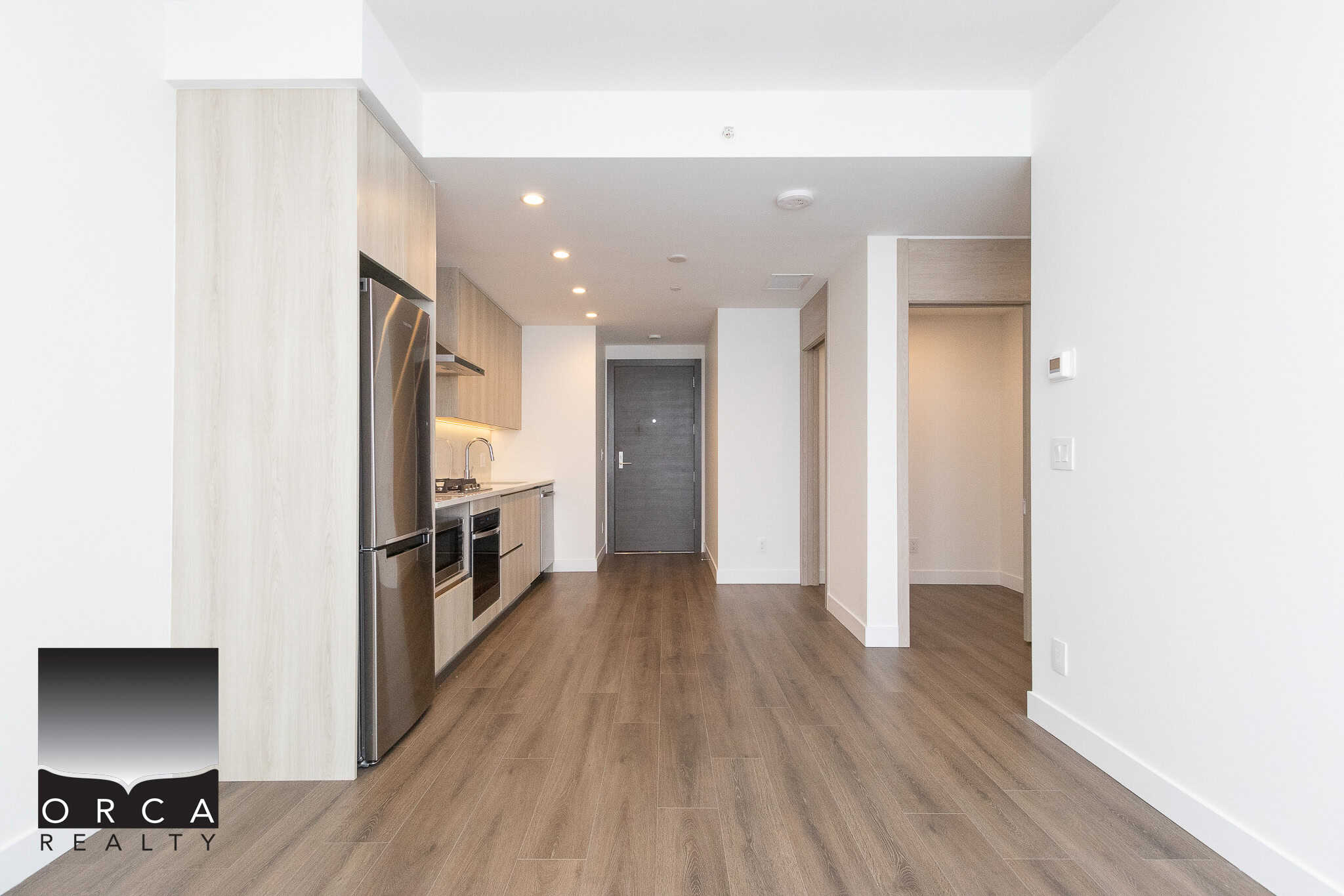 4 Modern open-concept kitchen in a new condo at Orca Realty Inc. with stainless steel appliances, light wood cabinetry, and hardwood flooring in Vancouver.