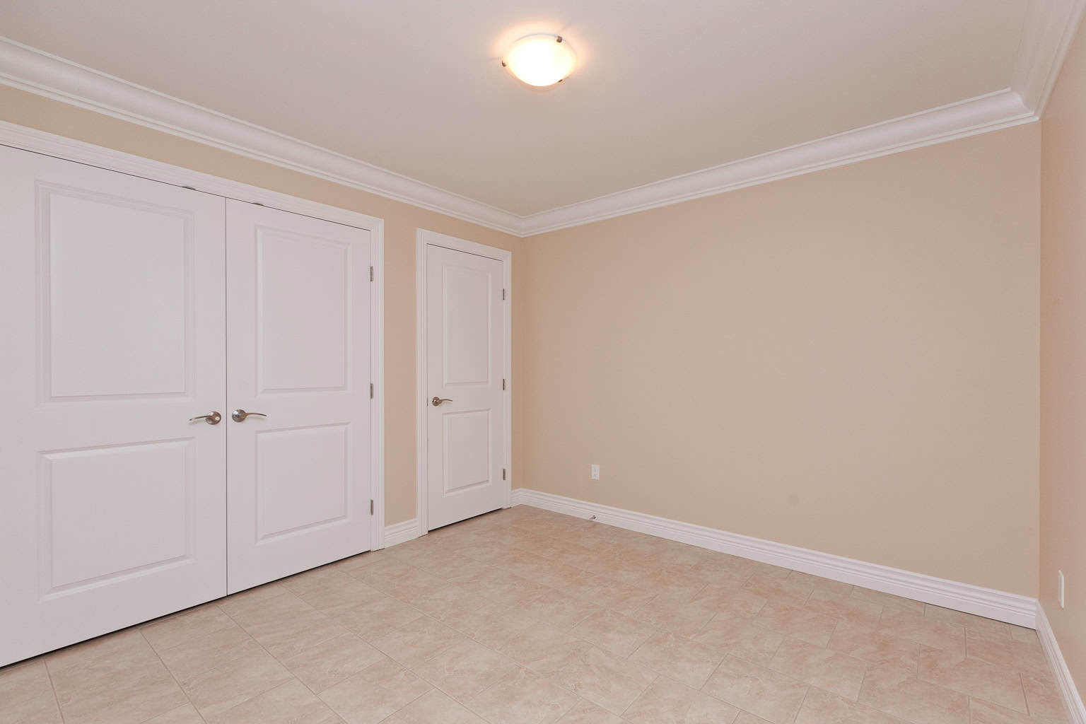 Bright empty room with beige walls, white trim, and double closet doors, ideal for residential living or real estate listing photos.