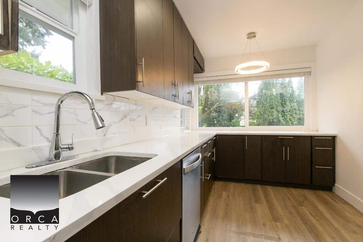 Modern kitchen with dark wood cabinets, white quartz countertops, stainless steel sink, and large window overlooking greenery, perfect for Vancouver Island real estate listings.