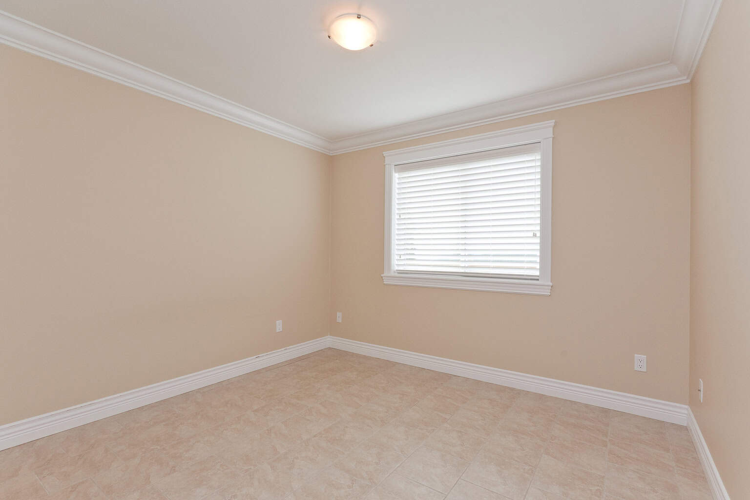 Bright empty bedroom with neutral walls, white trim, and large window with blinds, showcasing modern interior design for Vancouver homes.