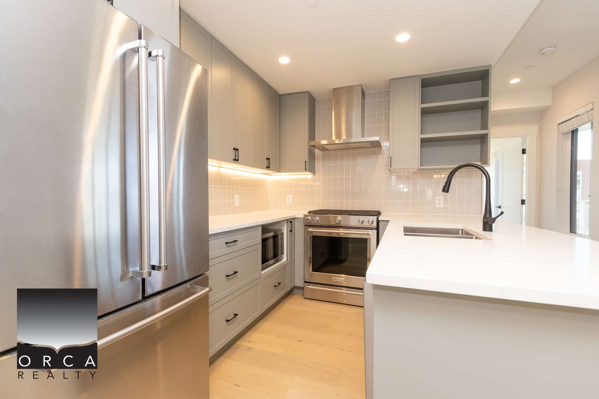 Modern grey kitchen with stainless steel appliances and white countertops, featuring ample cabinet storage, under-cabinet lighting, and a sleek design, ideal for Vancouver real estate listings.