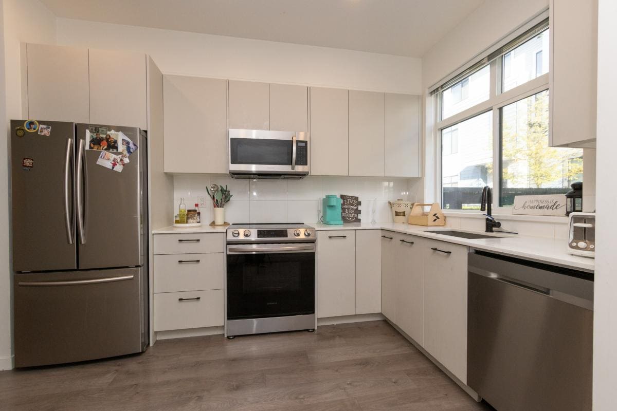 Modern kitchen with stainless steel appliances, white cabinetry, and large window for natural light, ideal for Vancouver real estate and property listings.
