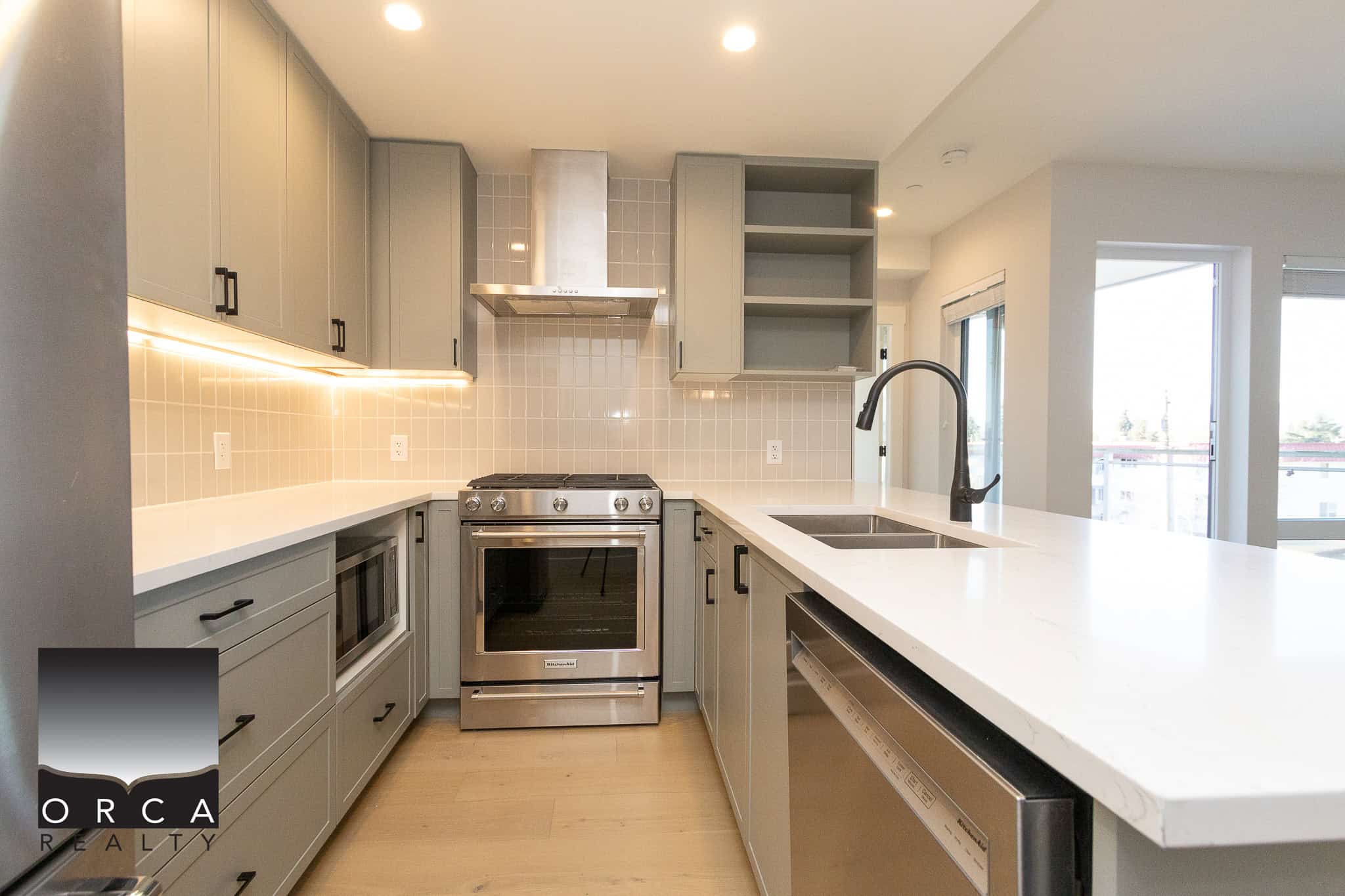 Modern grey kitchen with stainless steel appliances, quartz countertops, and open shelving in a contemporary home. Bright natural light, ideal for homebuyers seeking stylish and functional real estate in Canada.