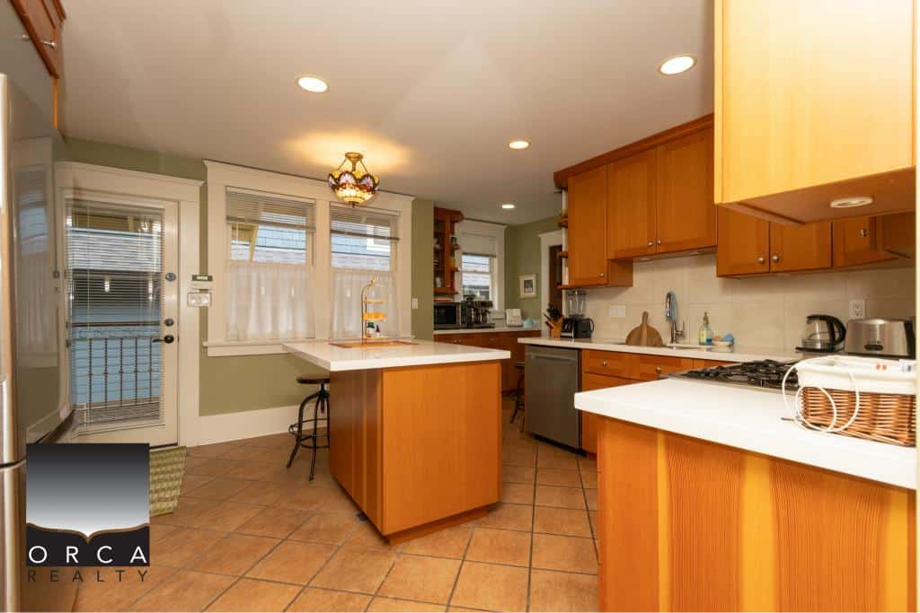 Modern kitchen with wooden cabinets and white countertops, featuring stainless steel appliances and natural light from windows; ideal for Vancouver Island real estate.