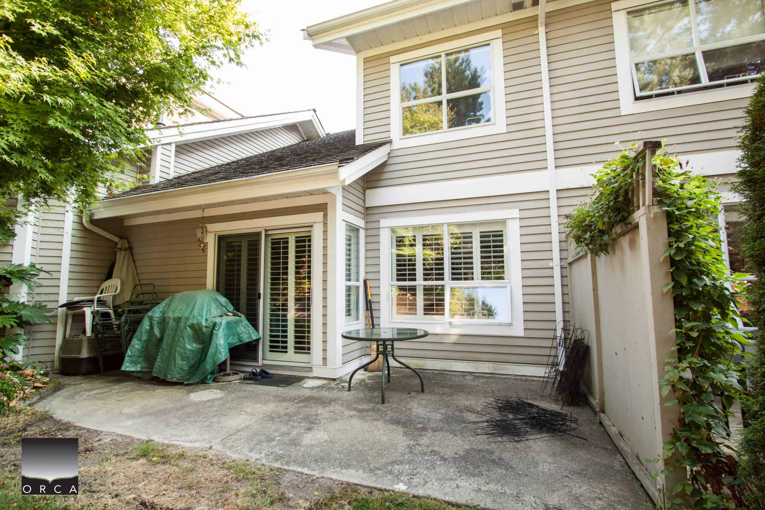 Spacious backyard patio with sliding glass door, outdoor furniture, gardening tools, and greenery, perfect for relaxing and outdoor gatherings in a family home or residential property.
