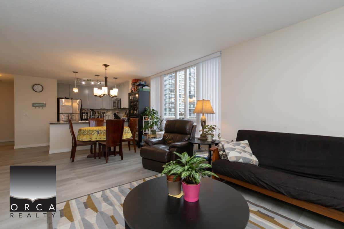 Bright living room and kitchen in a modern condo unit, featuring urban city views, contemporary furniture, and natural light, ideal for relaxed city living and real estate investment in Vancouver.
