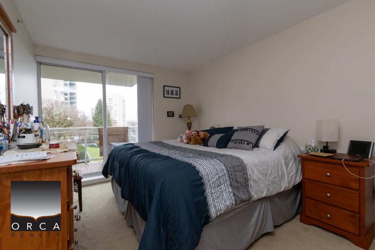 Bright master bedroom with large sliding door access to a balcony, featuring natural light, cozy decor, and peaceful urban views in a Vancouver-area condo.
