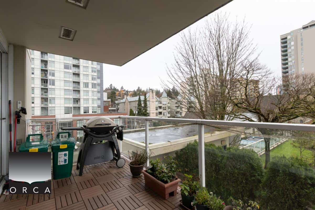 Spacious balcony with wooden decking, potted plants, and a BBQ grill overlooking a cityscape and greenery, showcasing urban living in Vancouver.