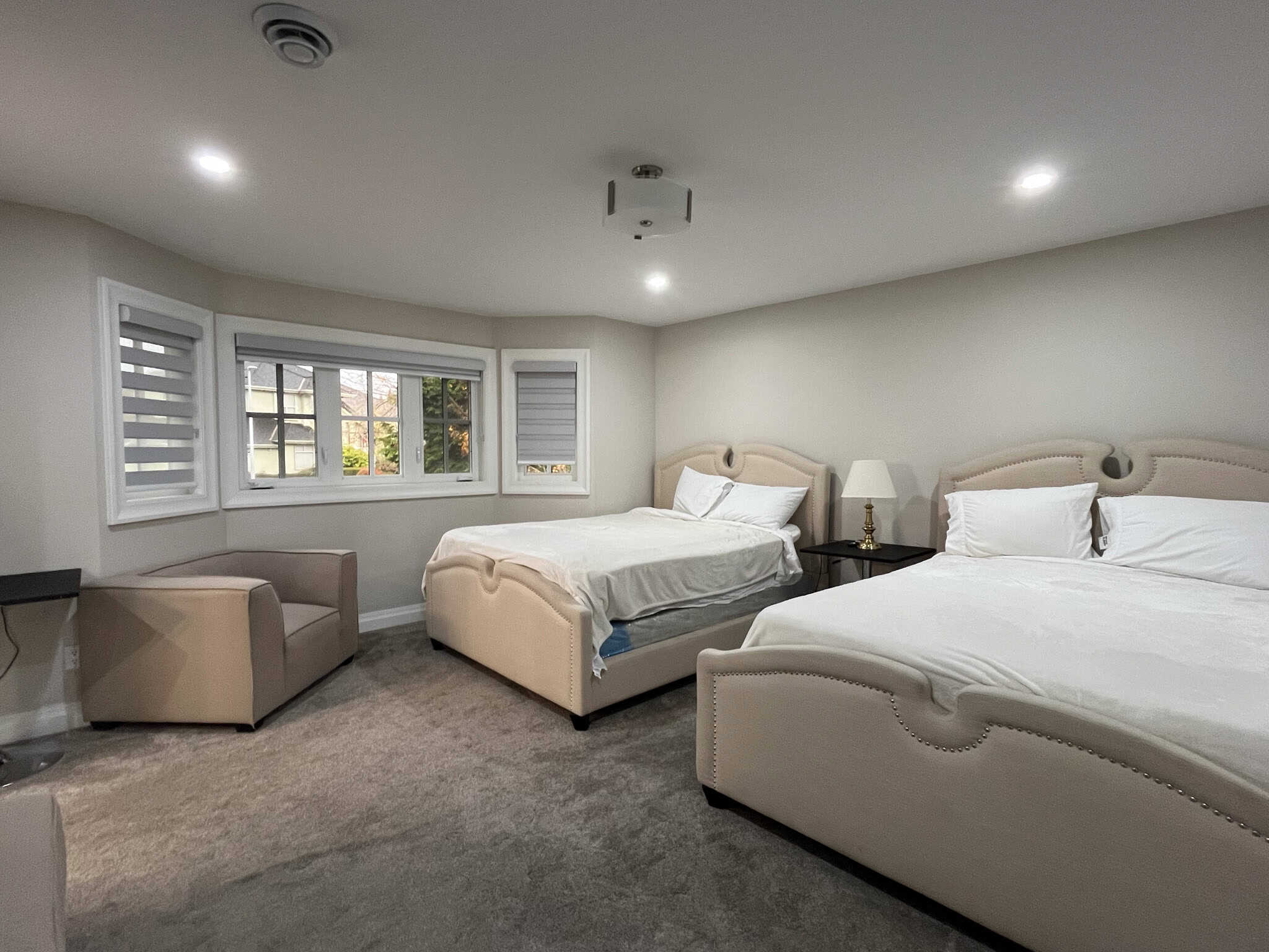 Spacious bedroom with two plush beds, neutral-toned decor, and large bay window offering natural light, perfect for Vancouver Island real estate listings.