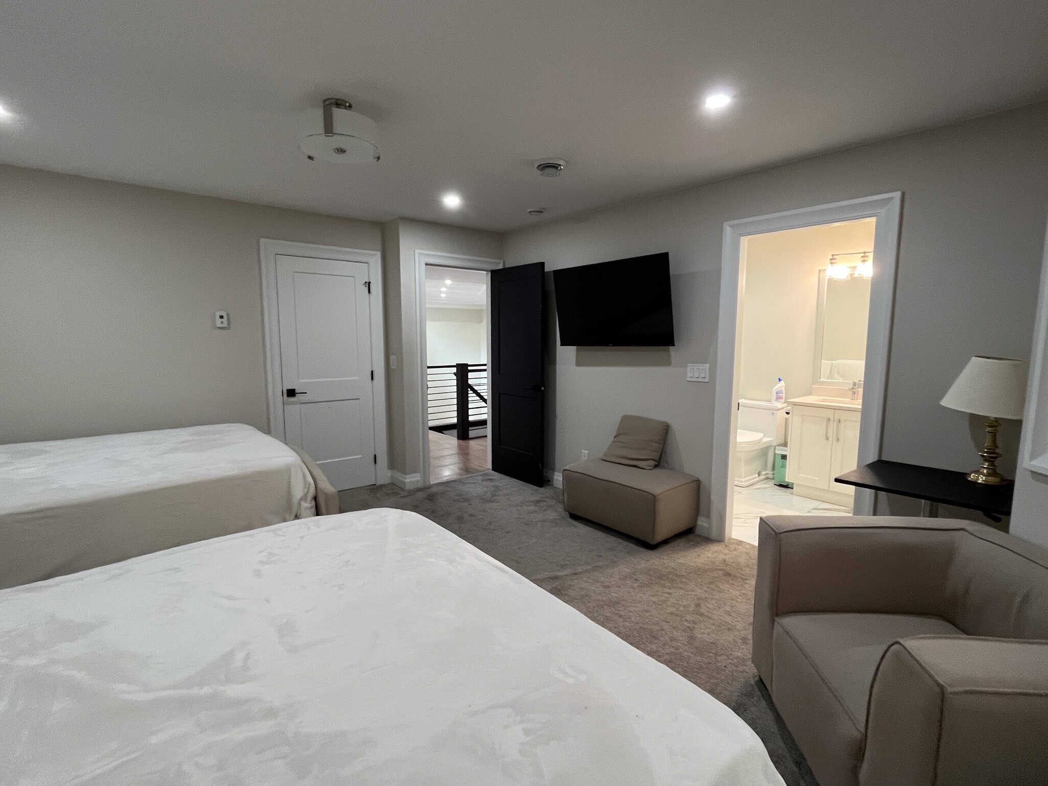 Spacious modern bedroom with two beds, mounted flat-screen TV, and comfortable seating area, perfect for relaxing or entertaining guests, in a contemporary home listed by Orca Realty Inc.