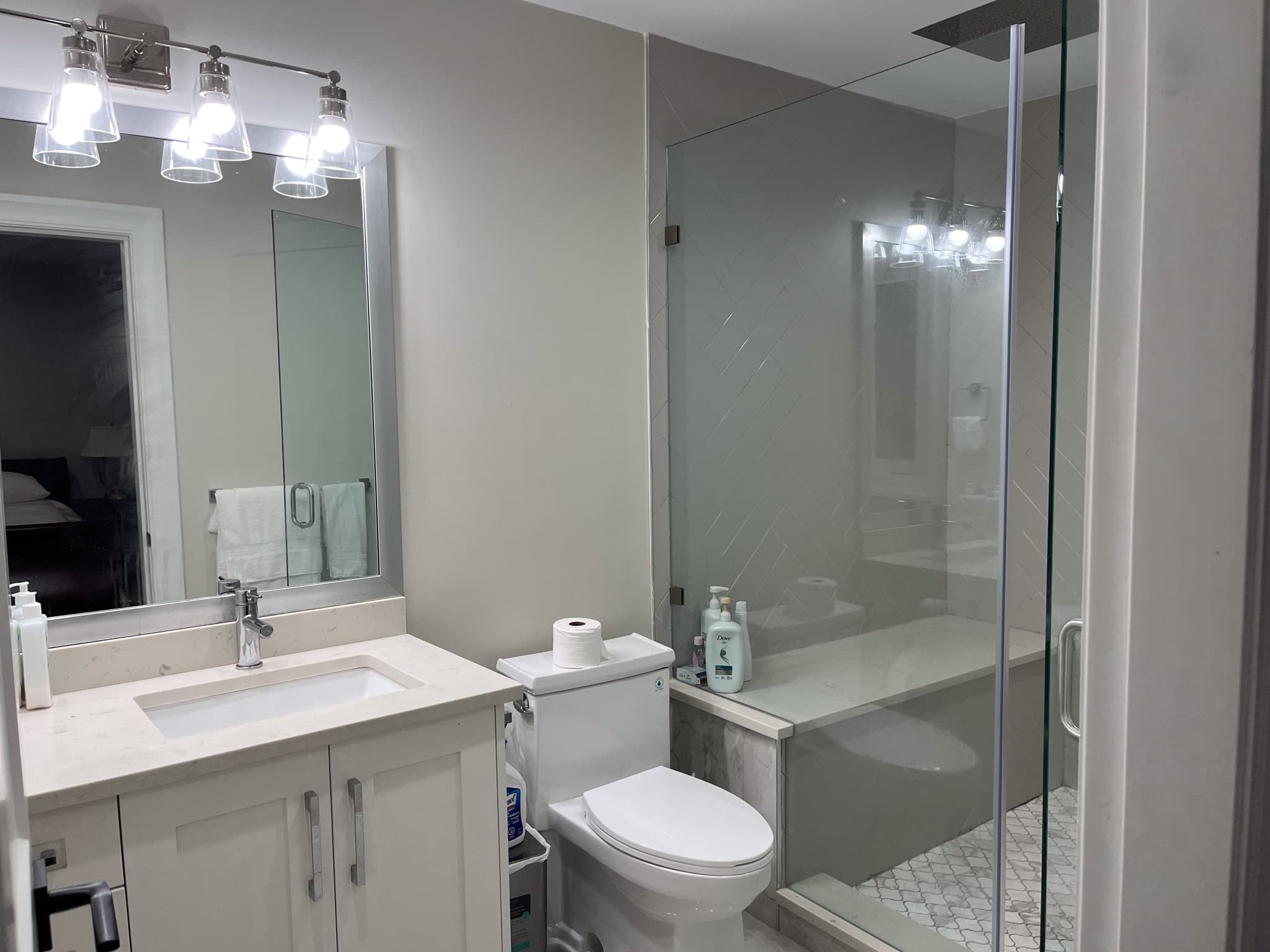 Modern bathroom with a sleek white vanity, large mirror, glass-enclosed shower, and contemporary lighting, showcasing upscale properties by Orca Realty Inc. for Vancouver real estate.