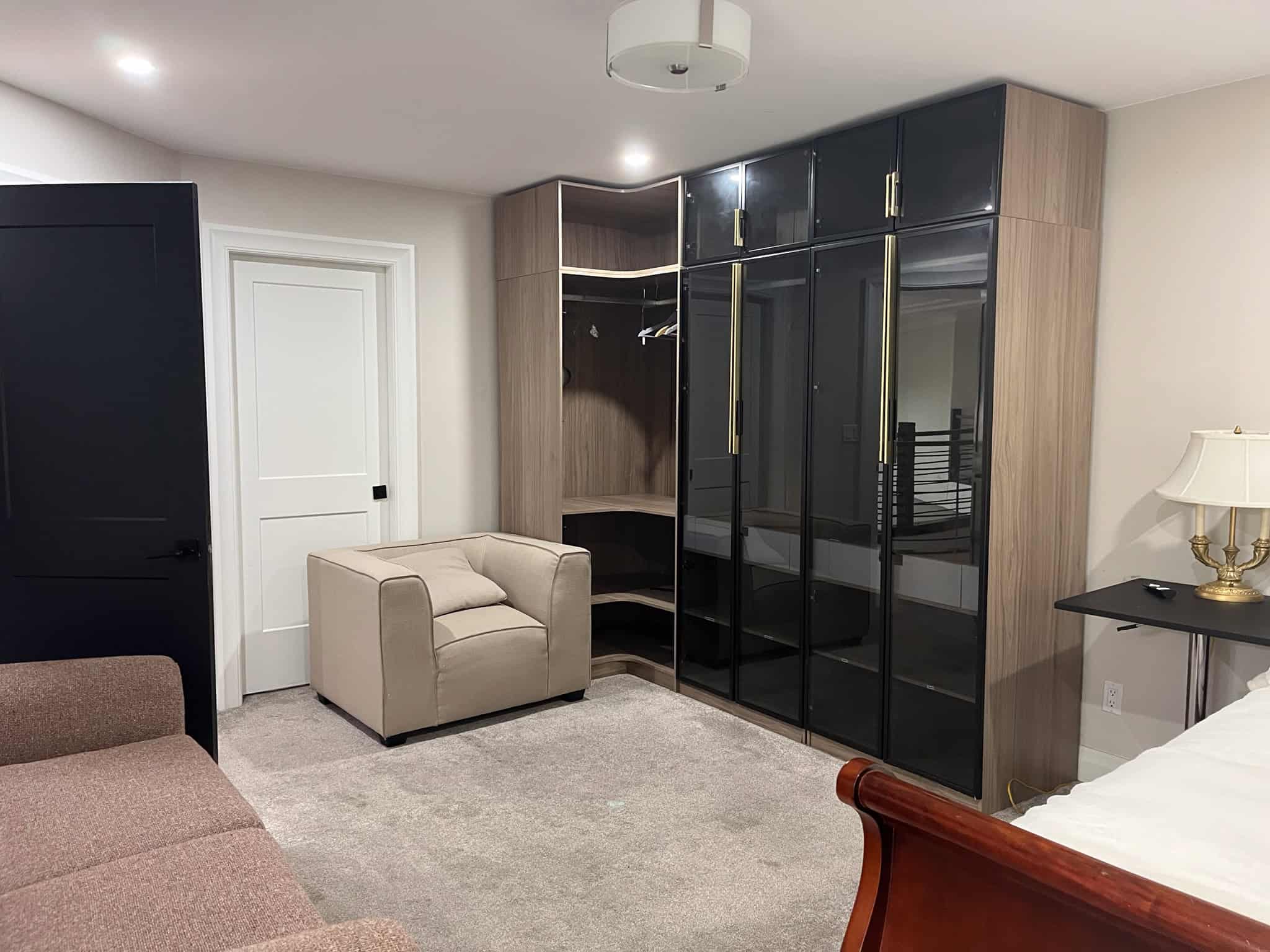 Luxurious bedroom features a built-in wardrobe with glass doors, cozy seating area, and elegant decor in a modern home. Perfect for relaxation and stylish living.