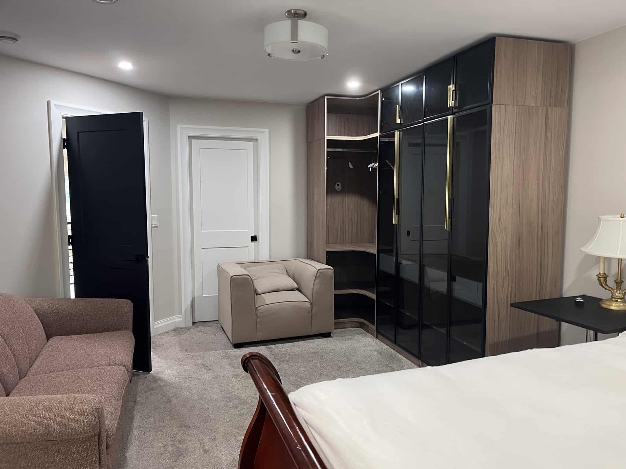 Modern bedroom interior with stylish black and wooden wardrobes, beige armchair, and cozy seating area, showcasing elegant home design and comfort.