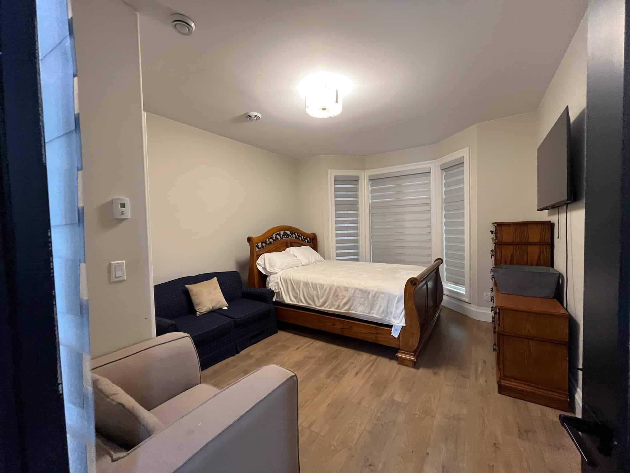 Cozy bedroom with wooden bed frame, large windows with blinds, and a mix of classic and modern furniture in a home listed by Orca Realty Inc.