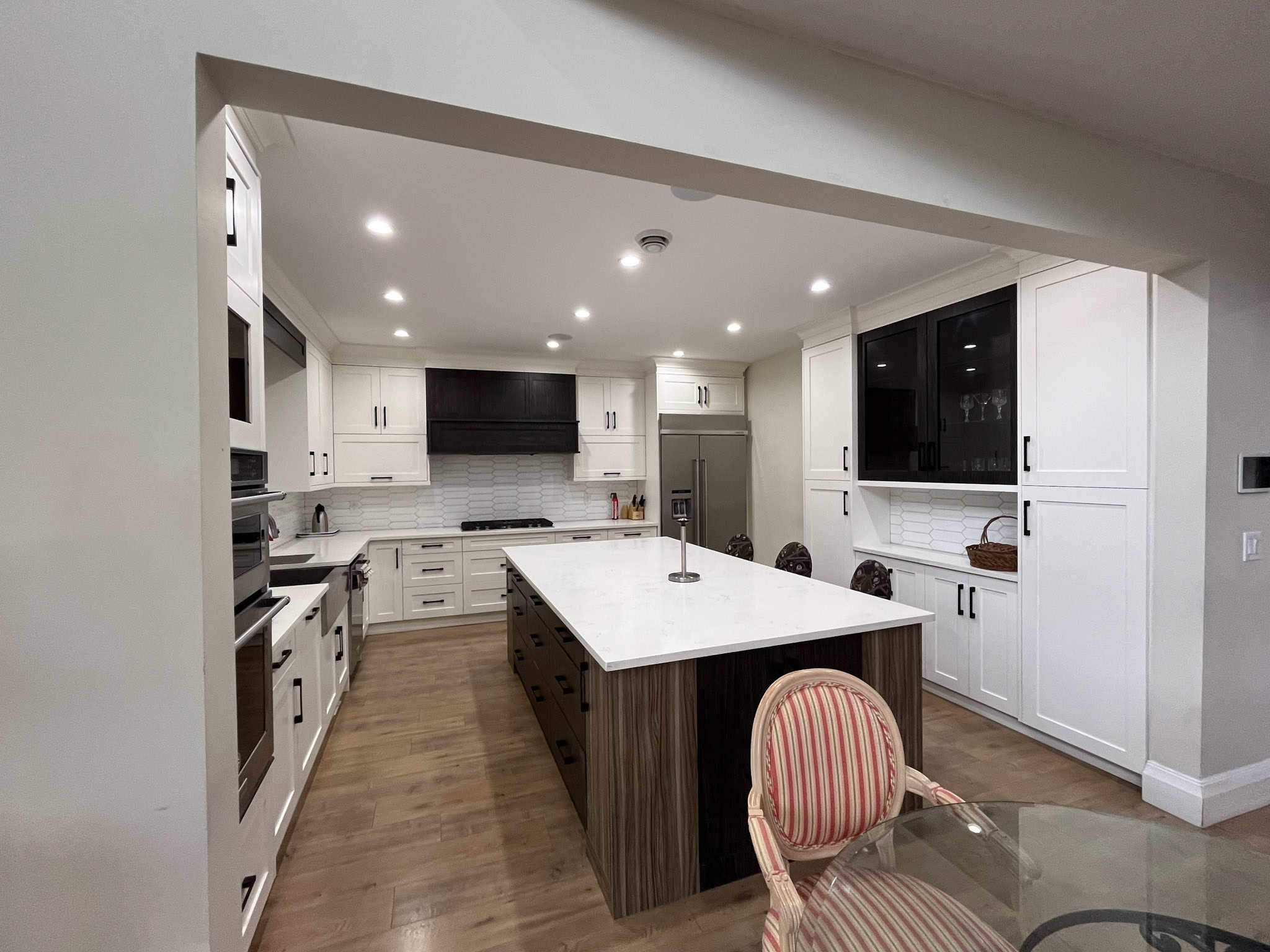 Contemporary modern kitchen interior with white cabinetry, island with dark wood base, stainless steel appliances, and elegant backsplash, ideal for luxury Vancouver Island homes.