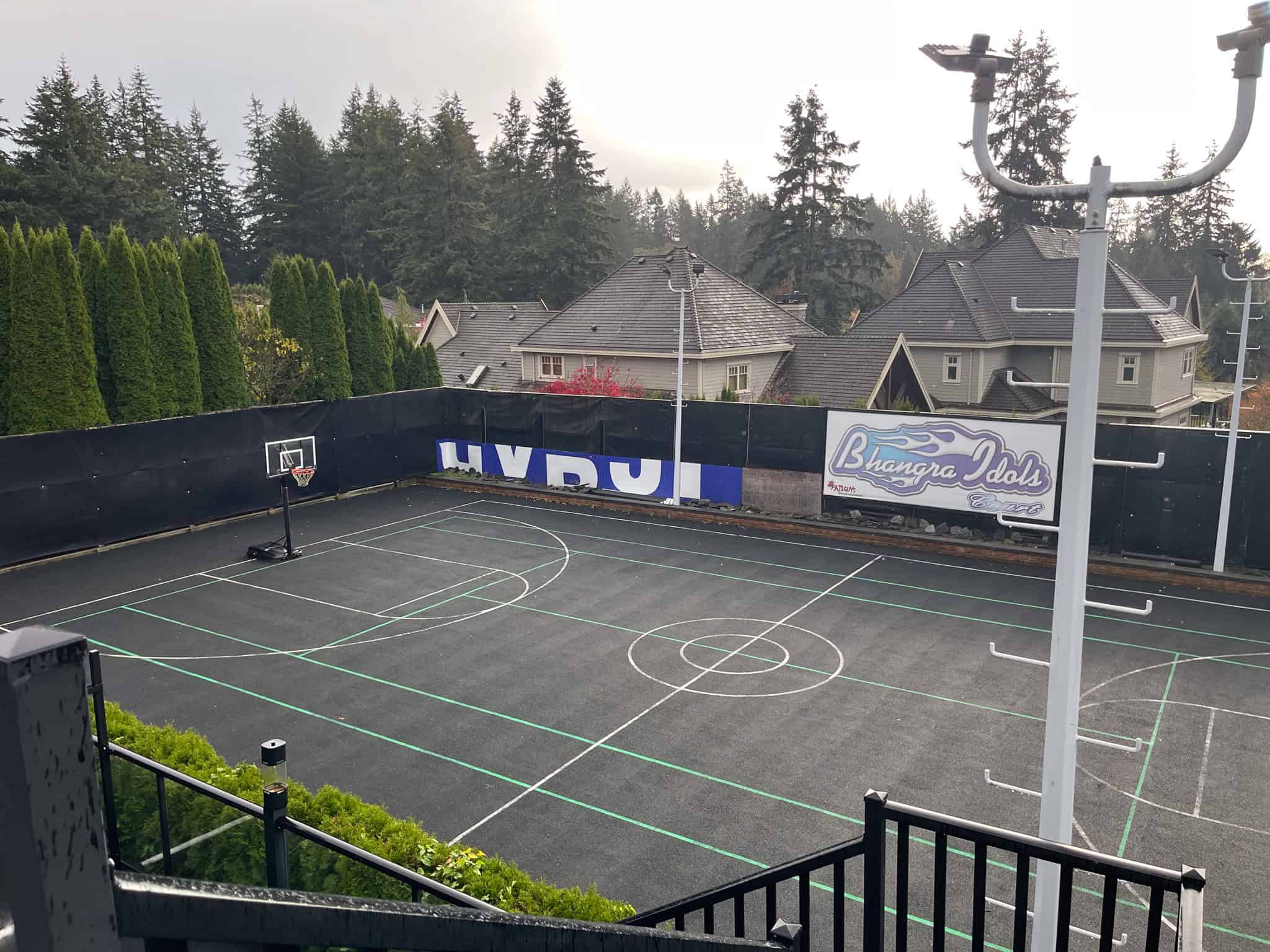 Modern outdoor basketball court at Orca Realty Inc. showcasing a professional-grade playing surface with hoop and boundary markings, surrounded by lush greenery and residential homes, perfect for recreational activities and community engagement.