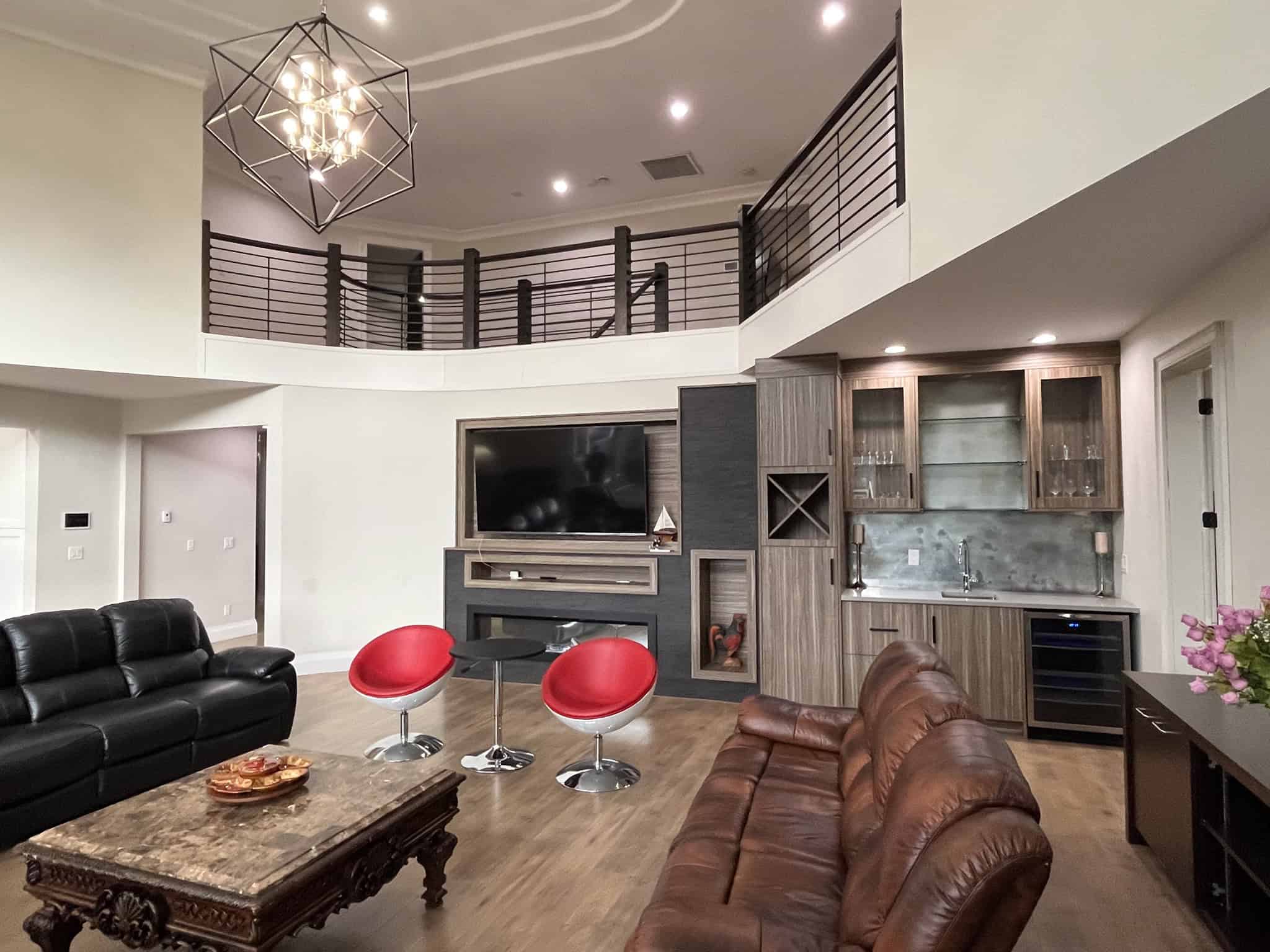 Modern living room with high ceilings, contemporary chandelier, and open plan design featuring a curved mezzanine, a flat-screen TV, stylish wooden cabinetry, leather and fabric seating, ideal for Vancouver real estate buyers.